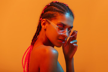 Beautiful young african naked woman posing isolated over yellow neon lights wall background wearing...