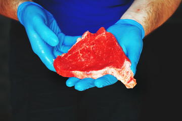 hands in blue gloves holding raw beef