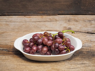Fresh red ripe grapes in white dish on wood texture background.