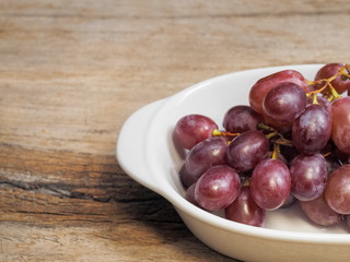 Close-up fresh red ripe grapes in white dish on wood texture background.