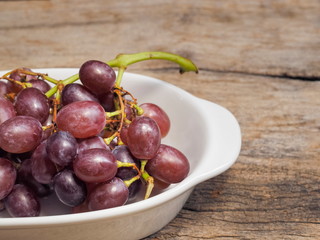 Close-up fresh red ripe grapes in white dish on wood texture background.