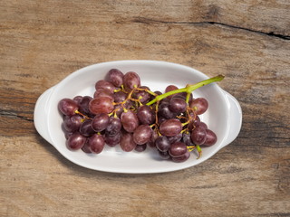 Top view fresh red ripe grapes in white dish on wood texture background.