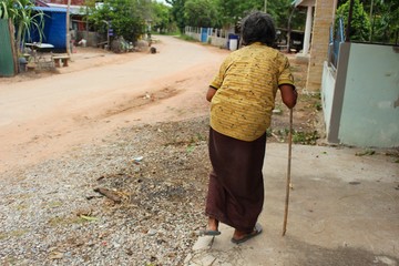 The old woman used the wooden support to walk on a rural road