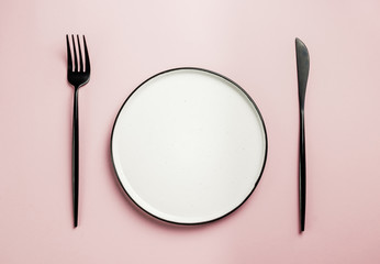 Black setting: plates, inen napkin and silverware on pink background. Top view.