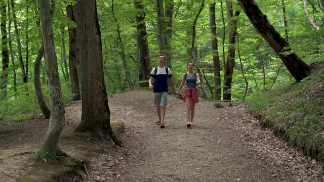 Guy and girl travelers go through the beautiful jungle forest with backpacks, holding hands, front view, outdoor activities concept, travel, Hiking