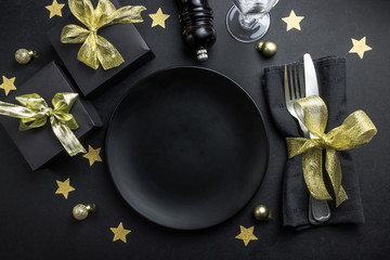 Christmas table setting with plate, silverware and decorations over black background