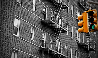 Green traffic light in New York city with an old urban building with fire escape stairs in the background. Selective color yellow. Black and white.