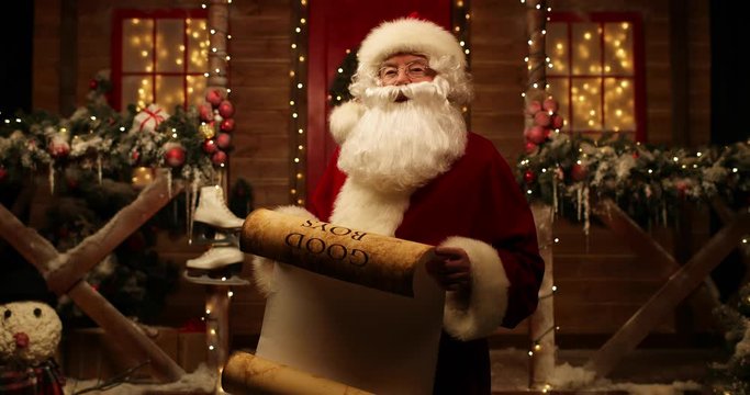 Santa Claus stands in the yard near his house and reads a scroll with the names of good boys and girls.