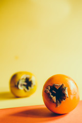 persimmon colored stil life, on a yellow orange board, autumnal fruit concept, lot of negative space to add a text.