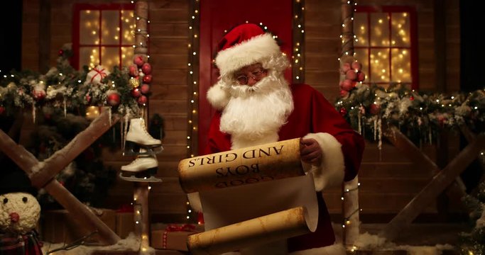 Santa Claus stands in the yard near his house and reads a scroll with the names of good boys and girls.