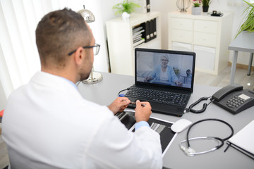 handsome doctor giving a remote medical consultation with senior woman patient over internet computer telemedecine diagnostic