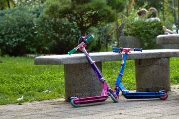 Two non-electric children's scooters parked on a concrete bench in the park.