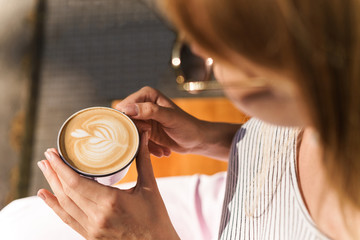 Cropped image of attractive young woman holding cup of coffee latte in cafe
