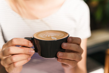 Cropped image of caucasian young woman holding cup of coffee latte in cafe
