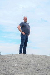 Forty something year old man standing tall on a hill with the blue sky and clouds in the background