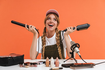 Image of young girl holding hair straighteners while recording blog broadcast about new cosmetic...
