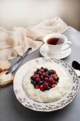 Delicious rice pudding with fresh berries and tea on a grey stone table