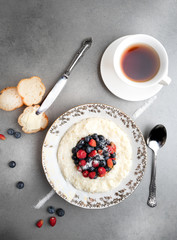 Delicious rice pudding with fresh berries and tea on a grey stone table