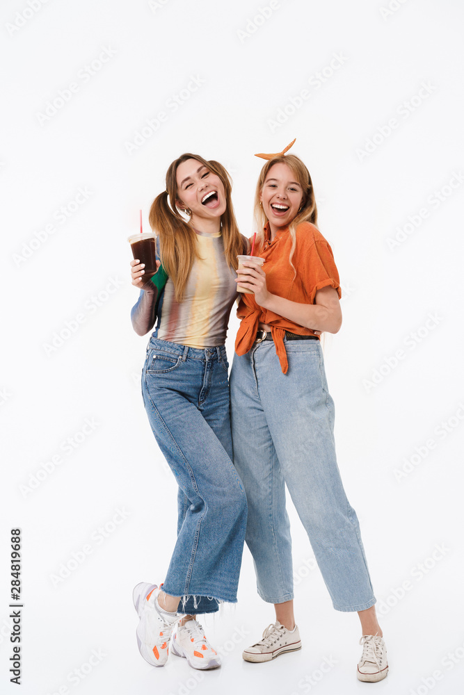 Canvas Prints Full length portrait of two young girls wearing casual clothes smiling and holding plastic cups