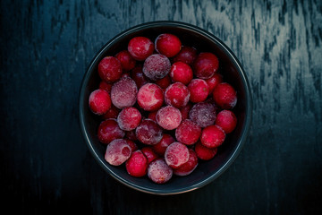 Frozen cranberries in a cup on a dark wooden background
