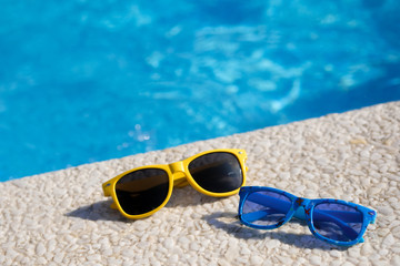 Fototapeta na wymiar Sunglasses lie on the background of the pool. Family travel. The best holidays for adults and children.