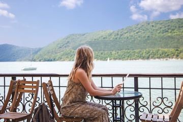 traveler blogger girl sitting in a cafe and looking at a beautiful mountain lake