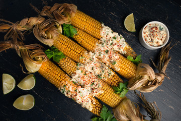 Baked corn cobs in a spicy sauce with lime on a dark background