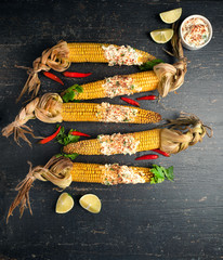 Baked corn cobs in a spicy sauce with lime on a dark background