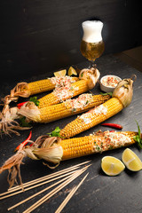 Baked corn cobs in a spicy sauce with lime on a dark background