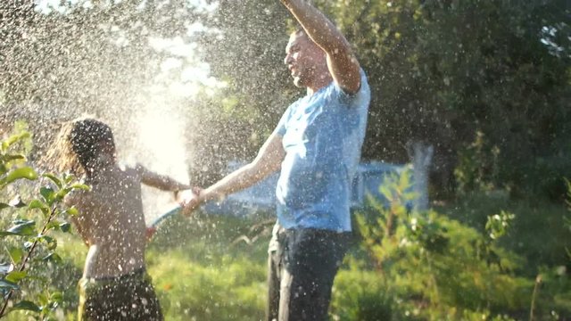 Curly-haired boy squirting his father with a hose. Holidays in the village, father's day