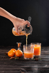 Fresh tangerines with cinnamon in a decanter on a dark background next to two glasses
