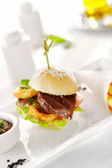 Gourmet, restaurant, delicious dinner food - close up of Sandwich with Beef and Deep Fried Onions Ring, Tomato and Cucumber. Garnished with French Fries