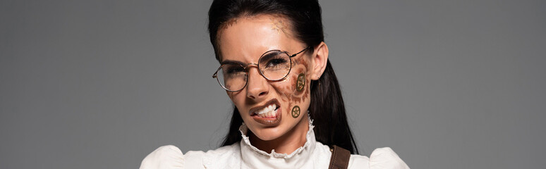 panoramic shot of irritated steampunk woman in glasses with makeup looking at camera isolated on grey