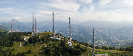 Drone aerial view of a group of towers for telecommunications, television broadcast, cellphone, radio and satellite on Linzone mountain peak. Electromagnetic and environmental pollution. Italian Alps