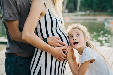 Image of man and girl hugging pregnant woman's belly on summer day