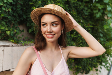 Smiling happy young pretty woman in beautiful hat walking by street.