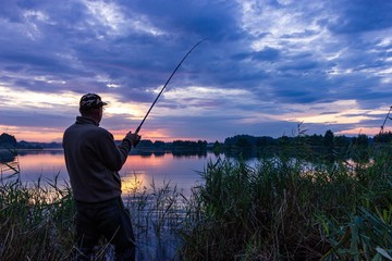 Angler catching the fish during cloudy sunset