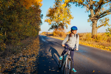 Young bicyclist riding on autumn field road at sunset. Happy woman traveler smiling