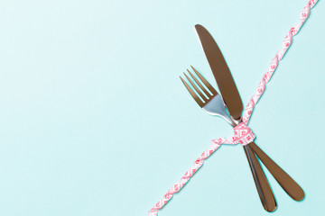 Diet and healthy eating concept with crossed fork and knife and curled measuring tape on blue...