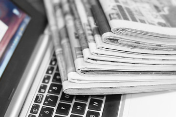 Newspapers and laptop. Pile of daily papers with news on the computer. Pages with headlines,...