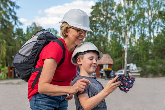 Outdoor profile portrait of a mother and boy child taking a selfie with mobile phone. Wearing white hard hats for urban exploration.