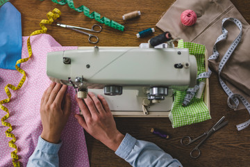 Seamstress using a sewing machine and various sewing accessories for clothes production. Top view