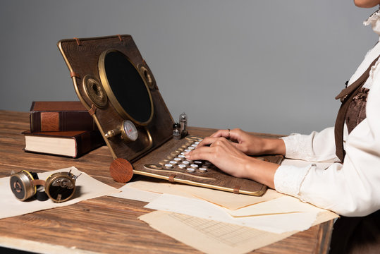 cropped view of woman typing on steampunk laptop at table isolated on grey