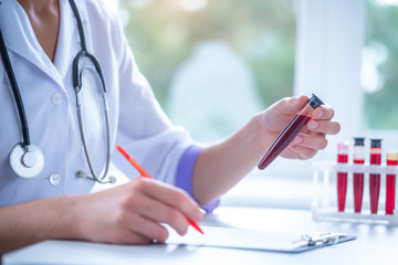 Professional general medical doctor examines blood sample from a vein and writes the results to the...