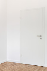 Closed white door with a gray chrome handle and keyhole with key against a white wall in the room