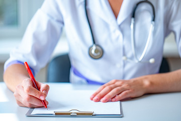 A doctor with a stethoscope writes out a medical prescription during a medical consultation. Health...