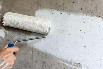 A painter paints a concrete wall with white paint, a male hand with a paint roller for painting a...