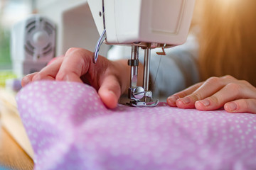 Female hands stitching fabric on professional manufacturing machine at workplace during sewing...
