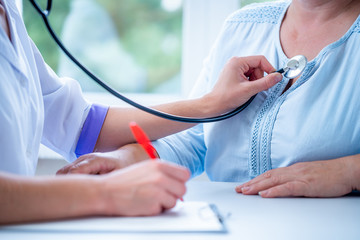 Professional general medical doctor listen lung and heartbeat of patient with stethoscope and write...