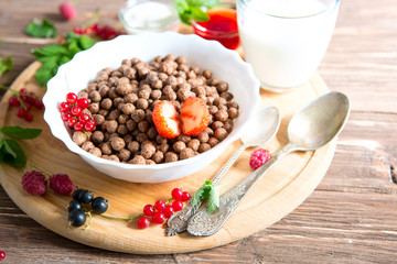 Breakfast pouring milk into corn flakes balls Healthy tasty breakfast chocolate balls with strawberries, raspberries, black currants and red currants.